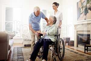 The life of a senior. Shot of a smiling caregiver with a senior woman in a wheelchair and her husband at home.