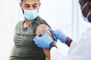 Gearing up for a global scale vaccination. Shot of a doctor applying a band aid after injecting a patient in his arm during a consultation at a clinic.