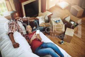 Who should we invite to the housewarming. Shot of a young couple taking a break while moving into their new home.