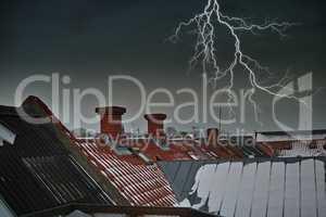 Thunder striking above chimney on red tiled roof. A dramatic lighting bolt in dark grey sky over a residential town with traditional slate roofing. Thunderstorm during a gloomy scary dark winter night