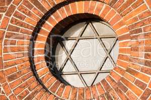 View of a pentagram sign and symbol on an old round window on a red brick wall. Vintage glass with metal frame and pentagon on historic church building and background. Architecture circular design