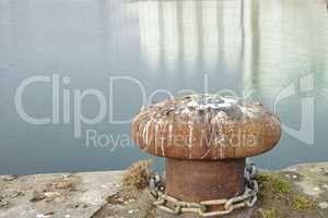 A bollard port by a harbour. Rusty mooring bollard cast iron at pier shore. Sky and water background copyspace. Securing anchor point to prevent vessels from drifting away due tide, current and wind