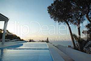 Scenic sunset view of an infinity swimming pool with an ocean background ocean. Luxury outdoor pool on a deck, patio, rooftop of a condo, home, hotel in the evening. Blue sky, horizon with copyspace
