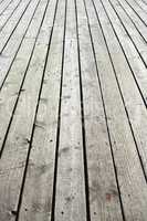 Closeup of a wooden plank surface. Light grey vintage flooring with slats forming an outdoor terrace. Old textures of hard wood floor used as a walkway or deck. Long vertical outdoor floorboards