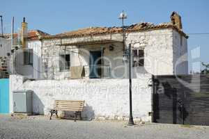 An old white farmhouse exterior. Ancient rustic house on the street with a broken damaged roof, tiny square windows and brick walls. Open windows in thick stone wall of an weathered antique building