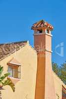 Chimney designed on roof of orange painted house building outside against blue sky background. Construction of exterior architecture of escape chute built on rooftop for fireplace smoke and heat