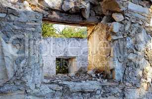 Abandoned old broken house with thick crumbling stone walls. Ruins of damaged rural home with an empty window frame. Weathered antique farmhouse with traditional architecture and building design