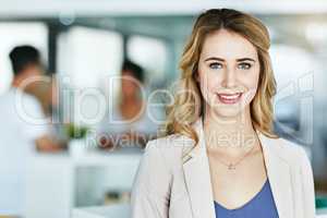 Im certain of my place in this business. Portrait of an ambitious young woman standing in a modern office with her colleagues in the background.