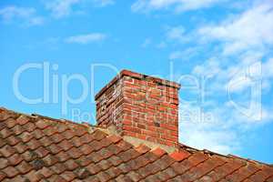 Red brick chimney designed on slate roof of a house building outside with cloudy blue sky background and copyspace. Construction of exterior escape chute built on rooftop for fireplace smoke and heat