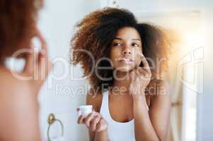 Making sure her skin stays hydrated all day. Shot of an attractive young woman applying moisturizer to her face in front of the mirror.