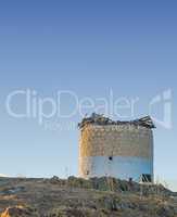 Old windmill in ruin on a hill with a scenic background of the blue sky. Ancient and historic design of a watermill display of vintage architecture. The exterior of an aged stone mill with copyspace