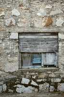 Wooden window boarded on an old rough stone wall farmhouse or ancient house. Vintage, rustic, old fashioned frame and shutters on historic village building. Antique architecture structure background