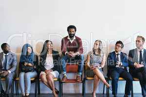 He is certain he will make the cut. Shot of a group of confident businesspeople waiting in line for their interviews while a man sits on top of a chair inside of a office during the day.