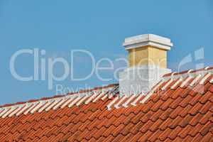 Brick chimney designed on slate roof of house building outside against blue sky background. Construction of exterior architecture of escape chute built on rooftop for fireplace smoke and heat