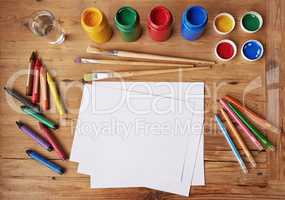 Creativity never goes out of style. Blank white paper with painting supplies and pencils on a wooden table.