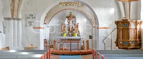 Interior of a historical church with rows of benches, a pulpit, nave or alter with kneeler cushions and sacred figure of Jesus on a cross. 12th century old Danish National Church in Faarup, Denmark