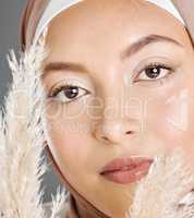 Closeup portrait face of beautiful young muslim woman wearing natural makeup and headscarf posing with pampas wheat plant against studio background. Glowing modest arab covered in traditional hijab