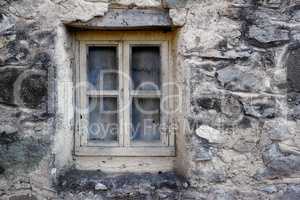 Closeup of a wooden frame window on ancient house in a village. Exterior of old dirty window and wall on farmhouse. A small window and grey stone or brick wall of an old antique building or cottage