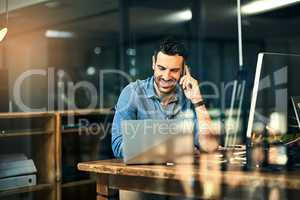 Inspiring productivity with a wealth of technology. Shot of a young businessman talking on his phone and using a laptop during a late night at work.