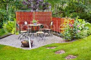 Chairs and a table in a beautiful garden or botanical area during spring or summer. Outdoor furniture in the backyard with lush green plants and flowers. A peaceful, serene, and private area at home
