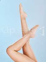 Closeup of unknown woman posing with her soft skin on her legs against a blue studio background. One female only feeling confident while showing her hairless, smooth legs after waxing or epilation