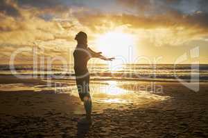 Rear View of a silhouette woman stretching with her arms out at the beach during sunset. Calm relaxed female feeling freed and enjoying a golden sunset out in nature. Golden sunset during dusk
