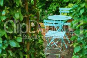 Two metal courtyard and patio chairs and table in serene, peaceful, lush, private backyard at home on a summers day. Furniture set and seating in empty, tranquil garden with fresh flowers and plants