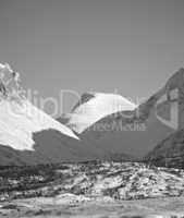 View of snow capped mountains and the glacier North of the Arctic Polar Circle in black and white. Open and empty mountain hill tops against clear sky. Monochrome of large mountains in Norway