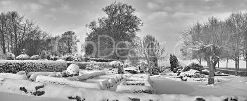 Gloomy graveyard in a monochrome winter landscape. Snow covered gravestones against a grey cloudy sky. Black and white empty frosted cemetery and frozen trees in greyscale. Snowfall in Scandinavia