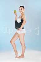 Beautiful woman holding scale and apple against blue studio background with copyspace. Portrait of one fit and happy young female showing weightloss progress from healthy lifestyle and balanced diet