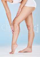 Woman stroking her shaved and smooth legs isolated on a blue studio background. Slim female touching her skin after hair removal, waxing or depilation treatment. Showing her beautiful long legs