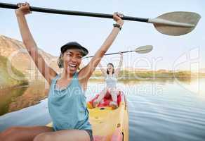 Portrait two diverse young woman cheering and celebrating while canoeing on a lake. Excited friends enjoying rowing and kayaking on a river while on holiday or vacation. Winning on a weekend getaway