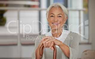 Portrait of a retired senior woman holding a wooden cane and smiling while sitting at home. Happy old lady leaning on a walking stick for support and enjoying her stay at a retirement facility