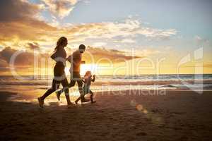 Silhouette of a carefree family running and having fun together during sunset on the beach. Parents spend time with their daughters on holiday. Little girl playing with her parents while on vacation