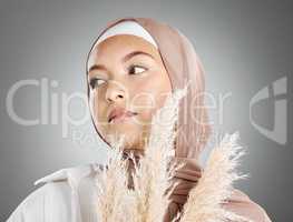 One beautiful young muslim woman wearing brown headscarf holding a pampas wheat plant isolated against grey studio background. Modest female arab wearing makeup with face covered in traditional hijab