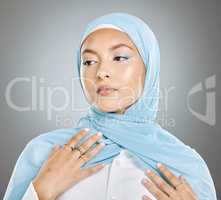 A glowing beautiful muslim woman isolated against grey copyspace background. Young woman wearing a hijab or headscarf showing her eyelash extensions while daydreaming, touching her flawless skin