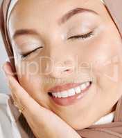 Closeup of beautiful muslim woman with eyes shut feeling satisfied with her skincare routine. Headshot of a stunning lady with glowing makeup and brown headscarf touching her face. Modesty and beauty