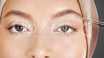 Closeup portrait of traditional muslim woman using tweezers to pluck her eyebrows. Half headshot of confident arab model wearing a hijab in a studio. Cultural middle eastern grooming her facial hair