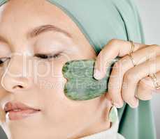 Muslim woman using a jade gua sha on face. Closeup headshot of an arab in a hijab sculpting face. Middle eastern woman using traditional chinese healing tool to aid lymph drainage, decrease puffiness