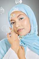 Studio portrait of one beautiful young muslim woman wearing blue headscarf against grey background with bubbles. Happy arab female wearing makeup with face covered in hijab for traditional modesty