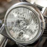 Closeup of a round headlight on a classic motorbike. One light bulb on a well maintained sliver chrome coated retro motorcycle. Motor vehicle accessories and parts. Glass lamp light with silver fram