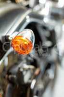 Closeup rear view of a taillight on a motorbike. Orange turning light on a blurred black vintage motorcycle. One modern chrome transportation vehicle. Maintenance on a shiny classic retro custom bike