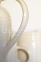 Abstract closeup of a porcelain teapot and cups. Concept of blurred white crockery and a set of kitchenware against an empty background. Ceramic coffee kettle handle with copyspace. Relaxing teatime