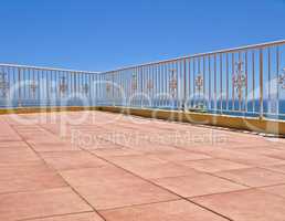 Beach house balcony or terrace with tiled floor and white fence. Summer view with a classic barricade overlooking the sea or ocean with a blue sky background. Seascape scenic view at a holiday lodge