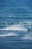 Calm waves in the empty ocean on a sunny day. Beautiful sea water with light ripple effects on the surface. Abstract aqua textures in the deep wide sea. White foam patterns in the Atlantic or pacific