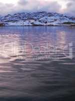 Copyspace of a calm sunset north of the Polar Circle on a calm winters day. Quiet Portage Lake with snow capped mountains on a cold winter day. An iced rural landscape in subzero temperature
