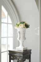 Still life of a bouquet of fresh white roses arranged with fruit and green leaves. Fresh flowers decorated with apples in a white antique vintage style clay vase next to a window on an antique table