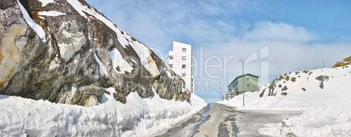 A snowy mountain road or street in a small town or city on a winter day. Empty urban location on a cold afternoon with ice on the pathway or roadway. White snow outdoors in a suburb in Europe