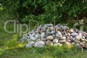 Stacked large stones or rocks on a field of green grass. Rocks along a remote hiking trail in nature. Collected pile of stones marking forest ground, symbolising a small grave on a hiking trail