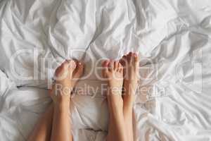 High angle shot of two unrecognisable womens feet relaxing together on the bed at home